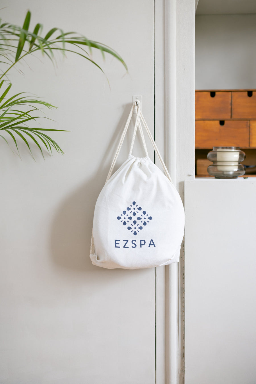 Die Baumwoll-Tragetasche von Ezspa mit dem Logo, aufgehängt in einem Schlafzimmer