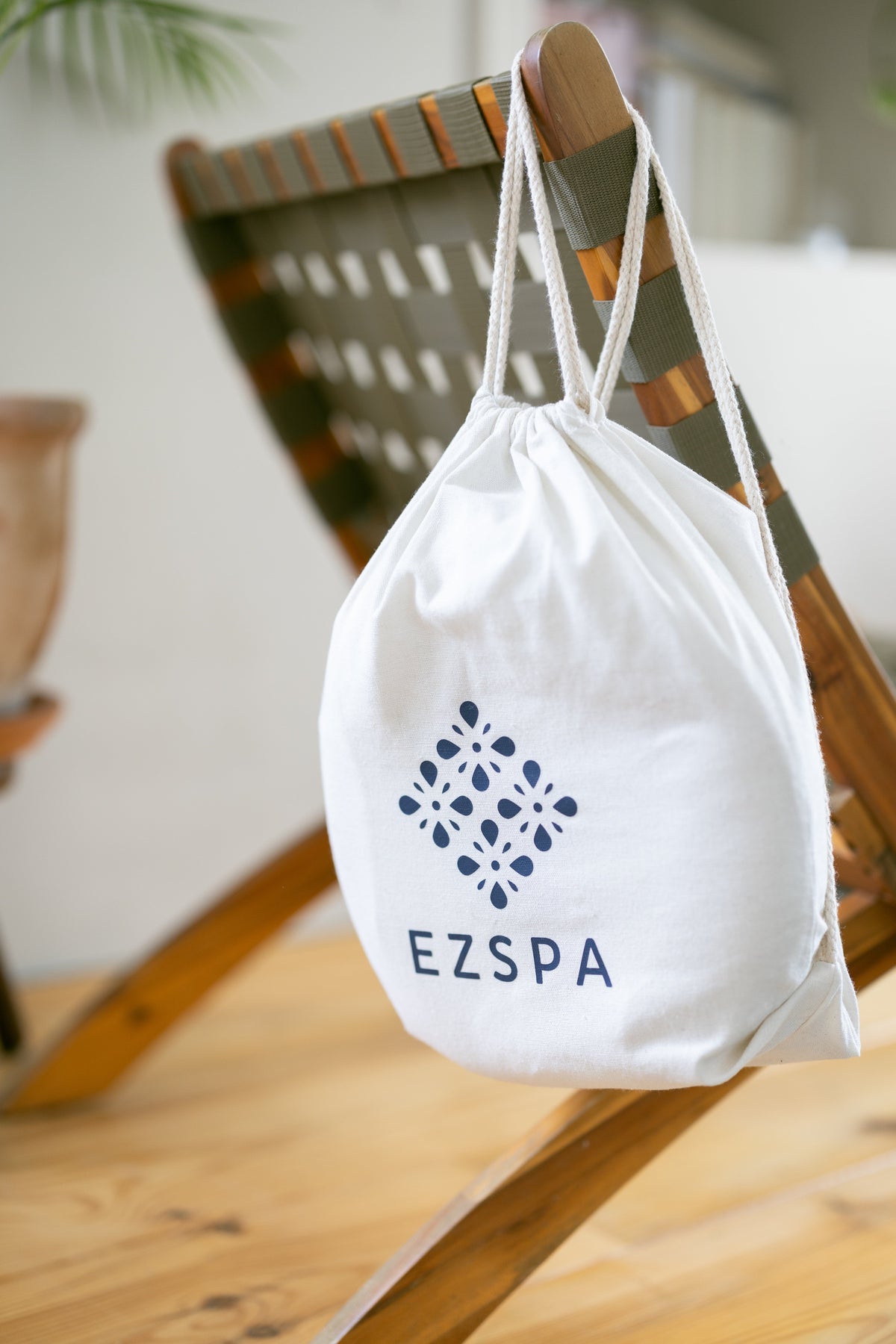 Die Baumwoll-Tragetasche von Ezspa mit dem Logo, hängend an einem Stuhl