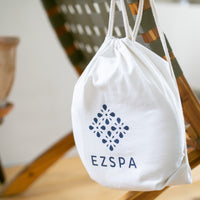 Die Baumwoll-Tragetasche von Ezspa mit dem Logo, hängend an einem Stuhl